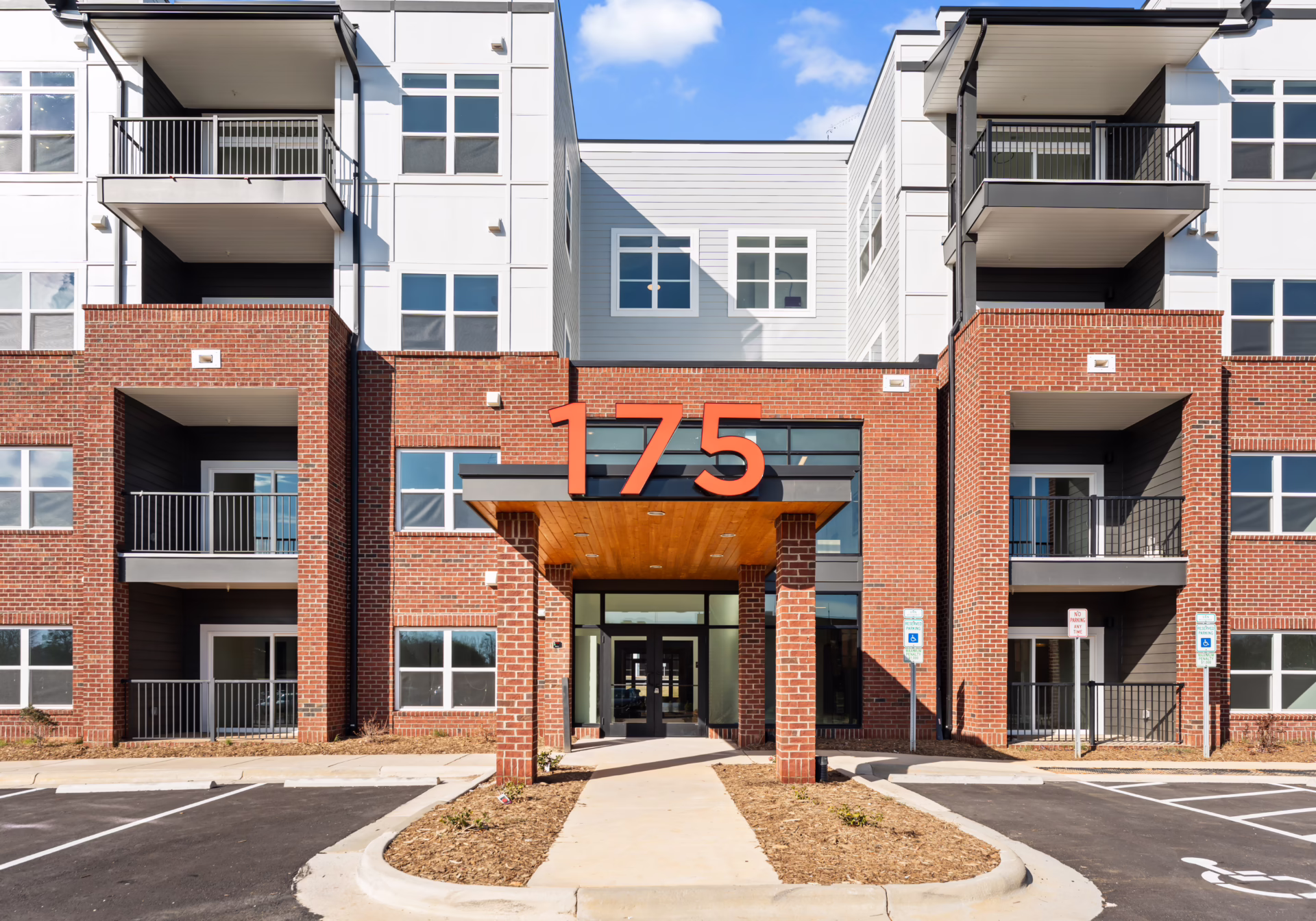 The main entrance of Brixton Apartments: red 175 numerals above a corten steel canopy, glass doors between brick piers.